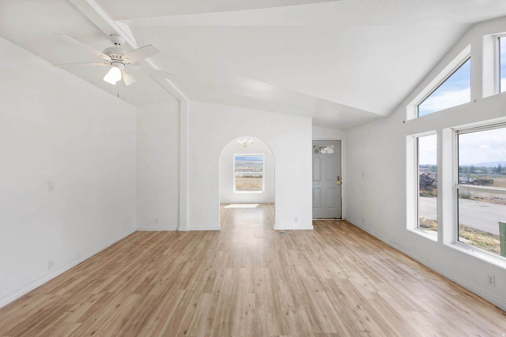 Vaulted ceiling, wood-finish flooring, white walls, ceiling fan, and large windows