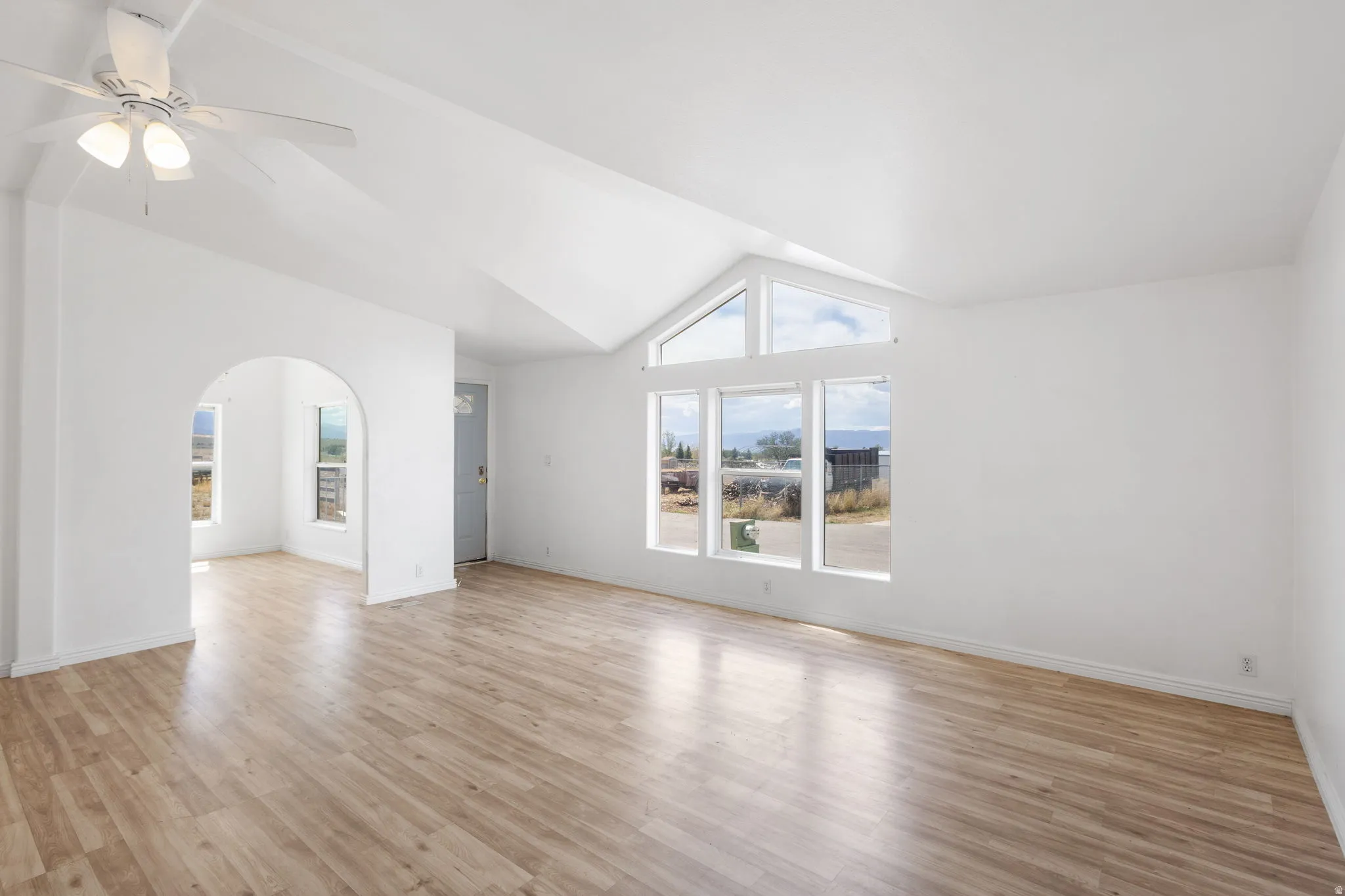 Vaulted ceiling with a ceiling fan, arched doorway, and wood-finish flooring