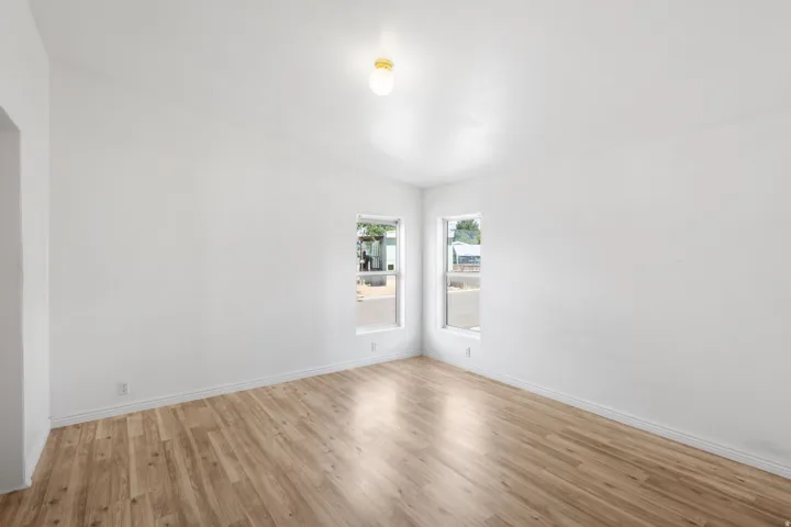 Vaulted ceiling, two windows, wood-finish flooring, white walls, and a ceiling-mounted light fixture