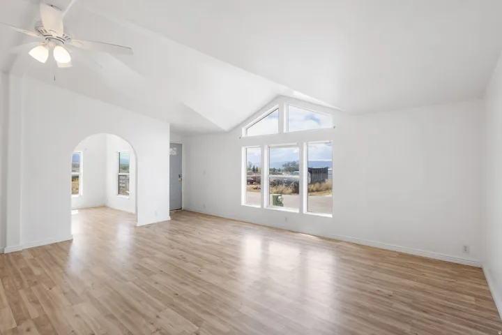 Vaulted ceiling with a ceiling fan, arched doorway, and wood-finish flooring