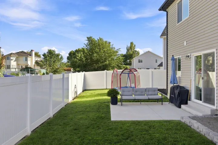 Spacious backyard featuring a manicured lawn, white privacy fencing, and a concrete patio