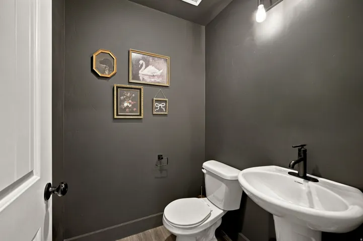 Pedestal sink with a matte black faucet, wall-mounted light fixture, and wood-finish flooring