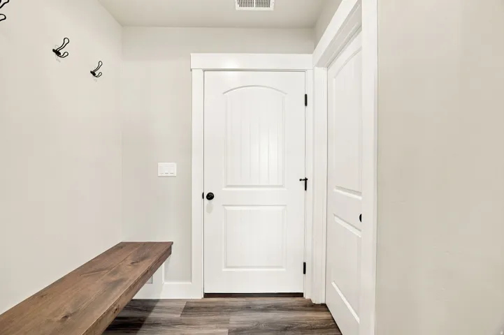 Entryway featuring wood-finish flooring, a built-in wood bench, and white panel doors with matte black hardware