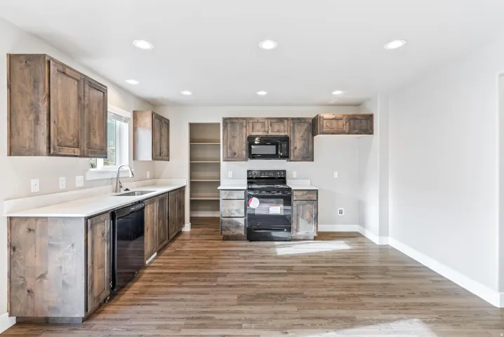 Wood-finish flooring, recessed lighting, wood cabinetry, light-toned countertops, and black appliances