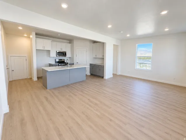 Open-concept layout featuring wood-finish flooring, recessed lighting, and a kitchen island with a stainless steel sink
