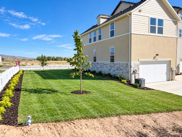 Expansive lawn area with a young tree, white picket fencing, and planted shrubs