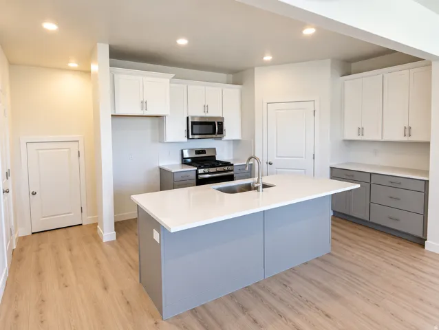 Kitchen featuring a central island with an undermount sink, stainless steel appliances, white upper cabinetry, grey lower cabinetry, and wood-finish flooring