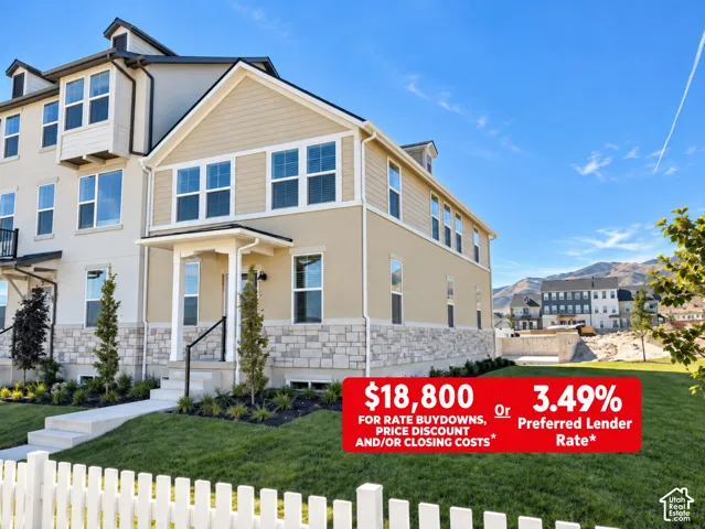 Multi-story residence featuring horizontal lap siding, stone veneer base, covered entry portico, and white picket fencing