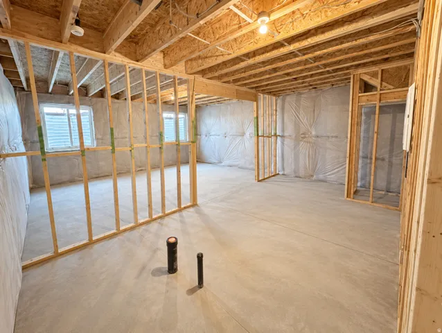 Unfinished basement space featuring exposed wooden framing, concrete flooring, and multiple egress windows
