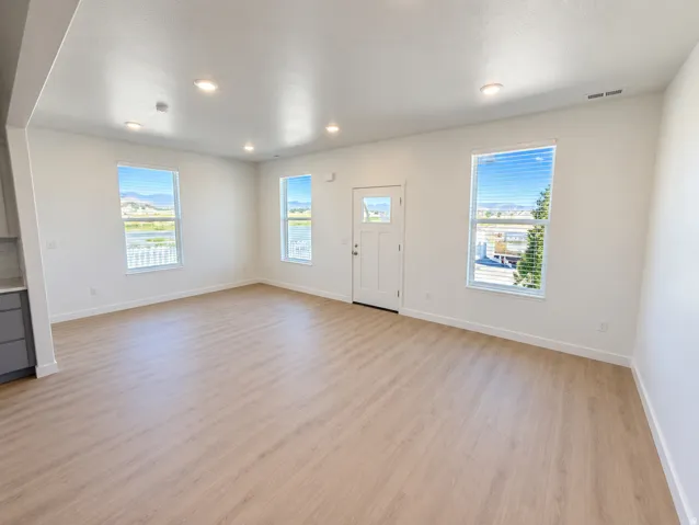 Recessed ceiling lighting, wood-finish flooring, white trim, white paneled door, and multiple windows with blinds