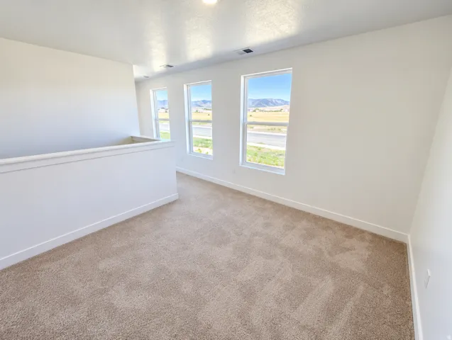 Recessed lighting, neutral tone carpeting, three large windows, and a partial height wall