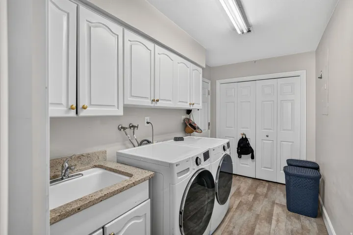 Built-in cabinetry with gold-toned hardware, utility sink with stone-finish countertop, and wood-finish flooring