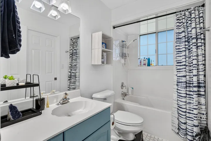 Bathroom featuring a white vanity countertop, blue-painted vanity cabinetry, a built-in bathtub, a window above the tub, and hexagon-patterned floor tiling