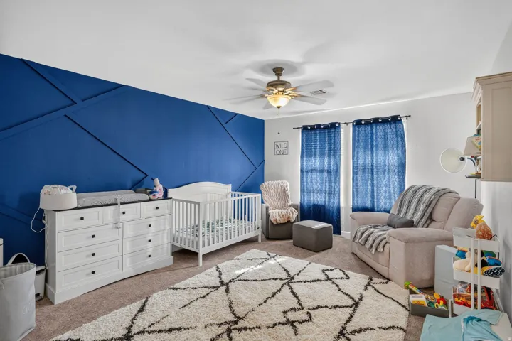 Accent wall with geometric paneling, ceiling fan with integrated lighting, carpeted flooring, and built-in shelving