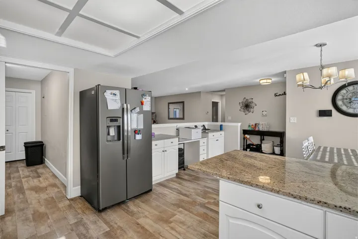Coffered ceiling detail, wood-finish flooring, white cabinetry, and a granite-finish island countertop