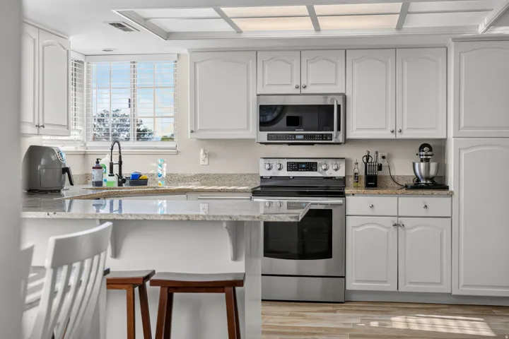 White cabinetry with brushed nickel hardware, light-toned countertops, stainless steel appliances, and wood-finish flooring