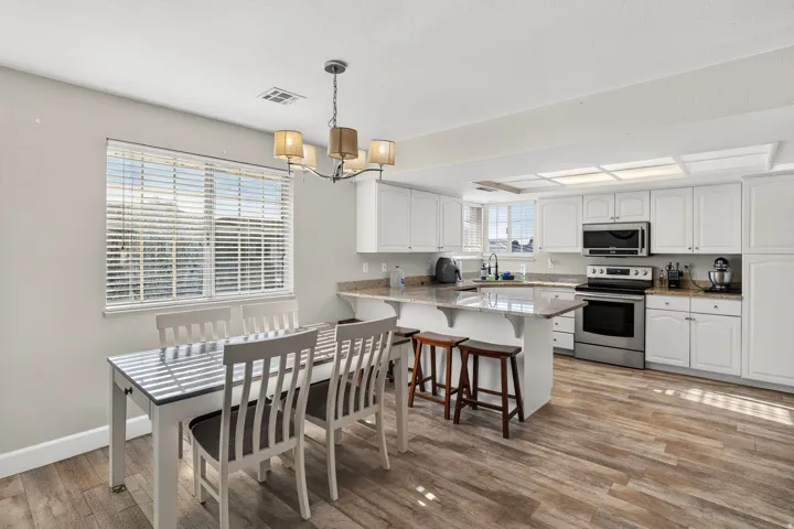Open-concept kitchen and dining area featuring wood-finish flooring, white cabinetry, stainless steel appliances, a kitchen island with seating, and a dining area with a multi-bulb chandelier
