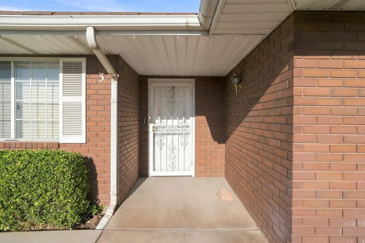 Brick exterior with white window shutters, a security screen door, and a covered entry