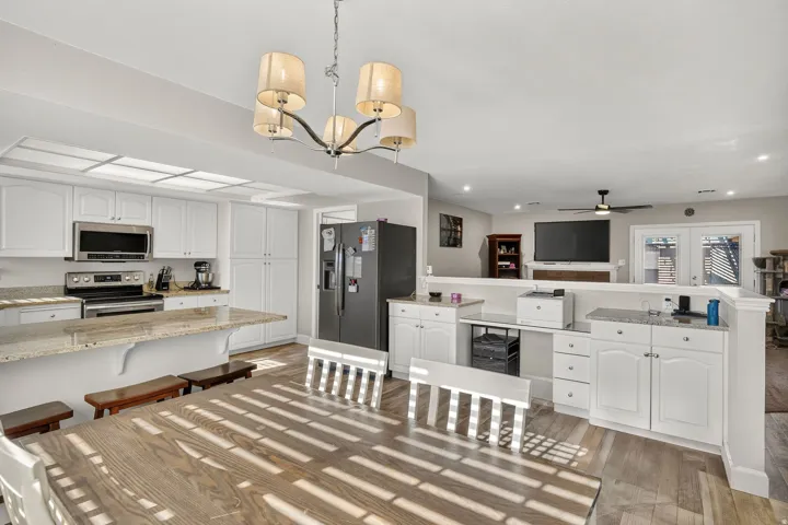 White cabinetry with stainless steel appliances, a kitchen island with seating, a decorative chandelier, and wood-finish flooring