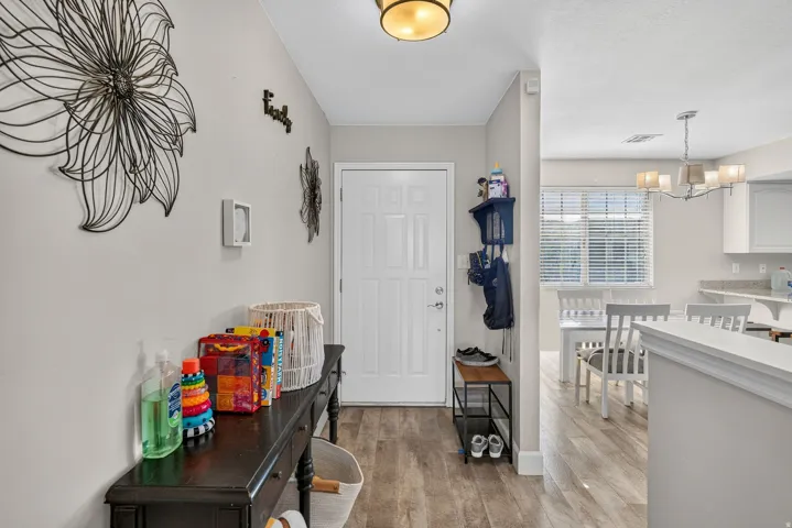 Wood-finish flooring throughout, white paneled door, flush-mount ceiling light, white window blinds, and a multi-arm chandelier