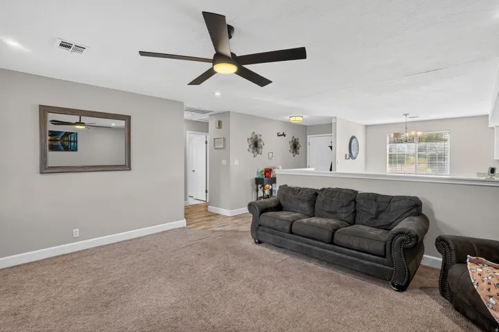 Recessed lighting and a ceiling fan fixture illuminate the carpeted living area, featuring a half-wall and wall-to-wall carpeting