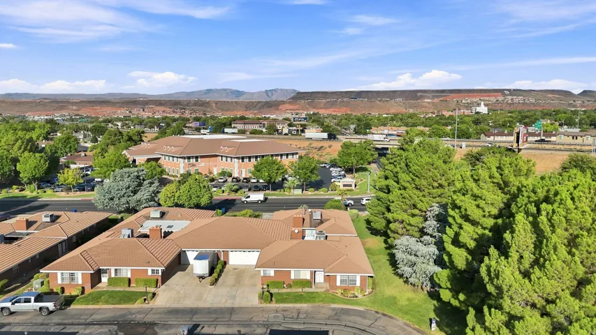 Red brick exterior, warm brown roofing, mature landscaping, paved driveways, and mountain backdrop