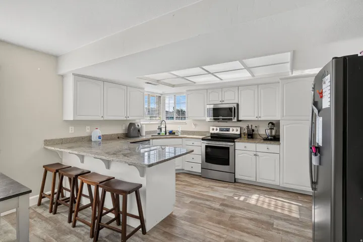 Kitchen featuring white cabinetry, light-toned countertops, stainless steel appliances, and wood-finish flooring