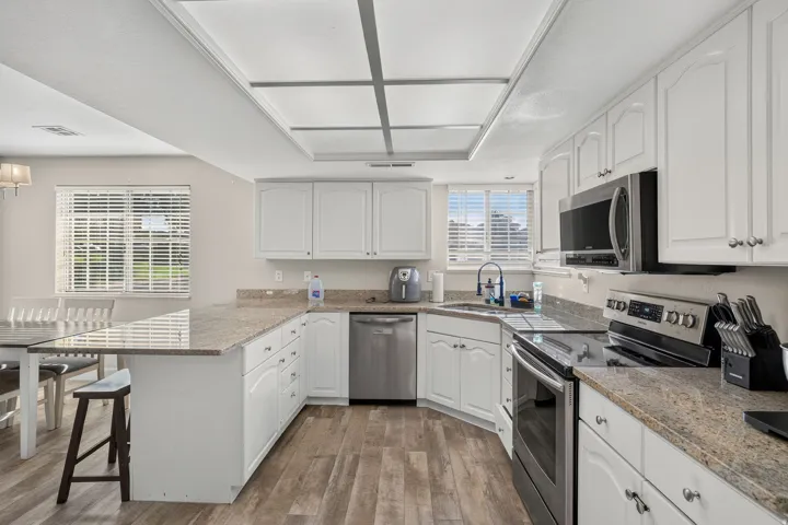 Kitchen featuring white cabinetry, granite-finish countertops, stainless steel appliances, wood-finish flooring, and a built-in kitchen island