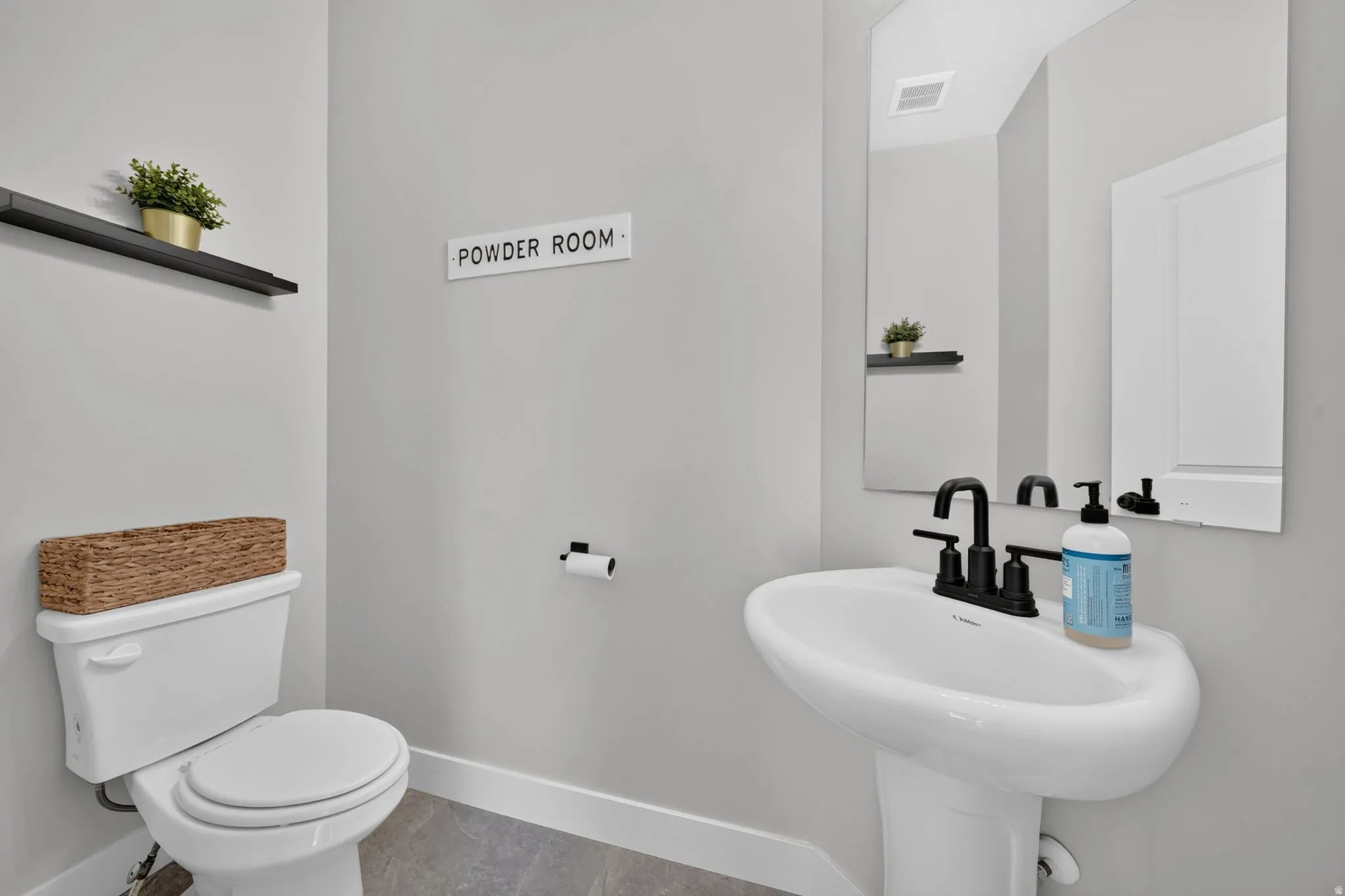 Pedestal sink with a matte black faucet, wall-mounted mirror, and tile flooring