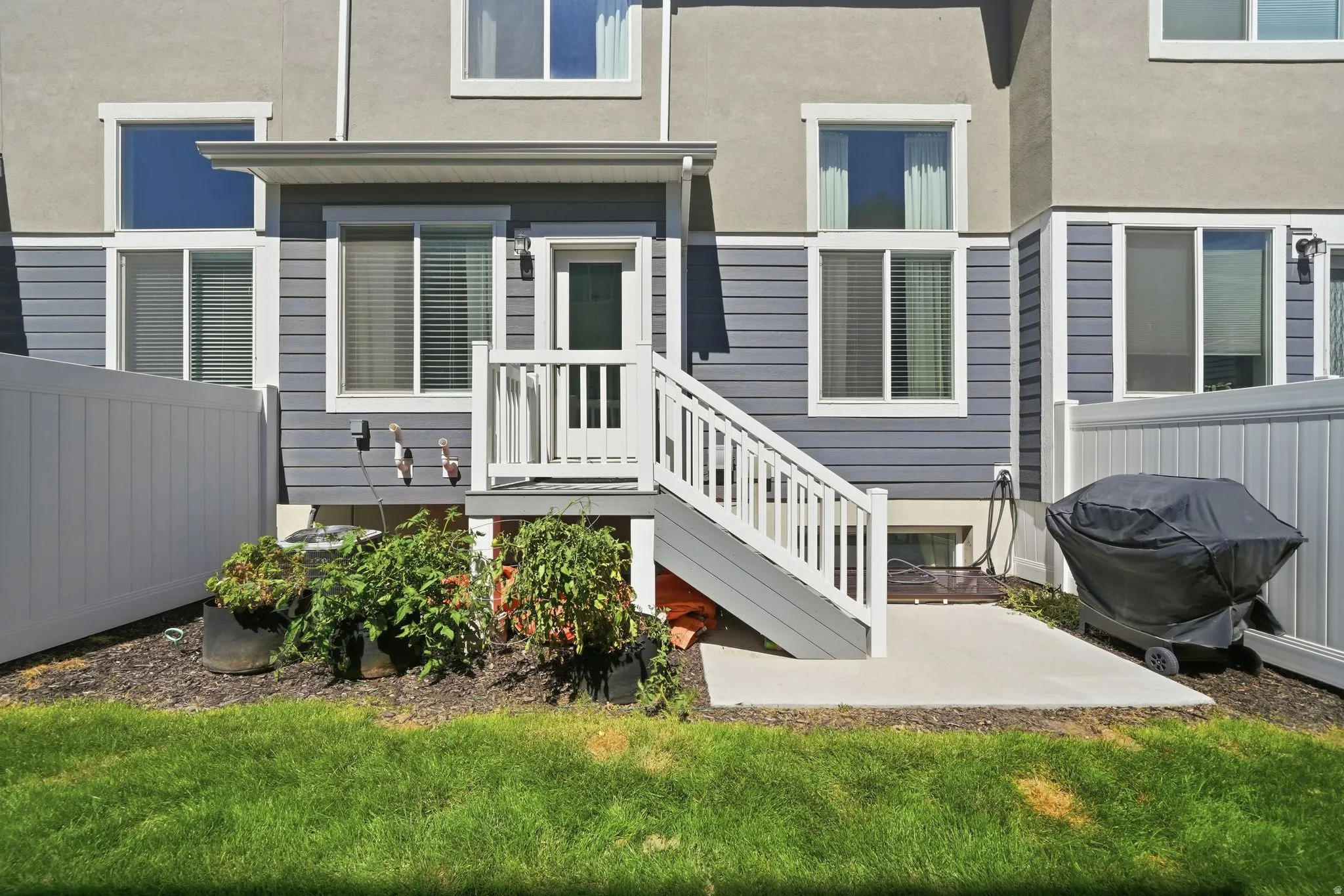 Exterior featuring gray siding and light stucco, an upper-level patio door, and white railing steps to a ground-level concrete patio