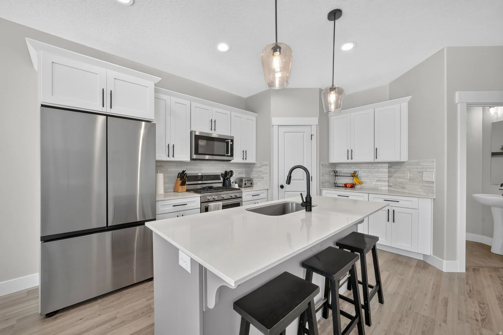 White shaker cabinetry, stainless steel appliances, central island with seating, pendant lighting, and wood-finish flooring