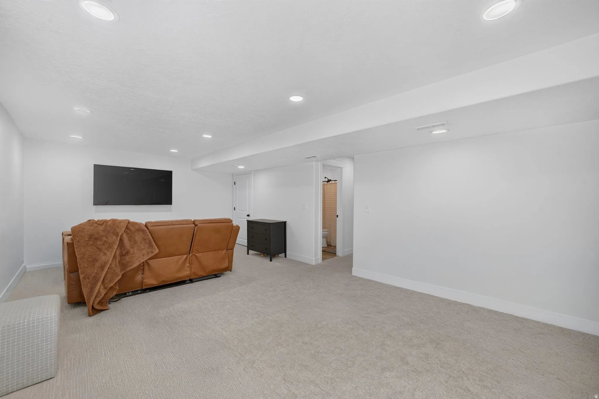 Recessed lighting, light-toned carpeting, white walls, and a white door with black hardware
