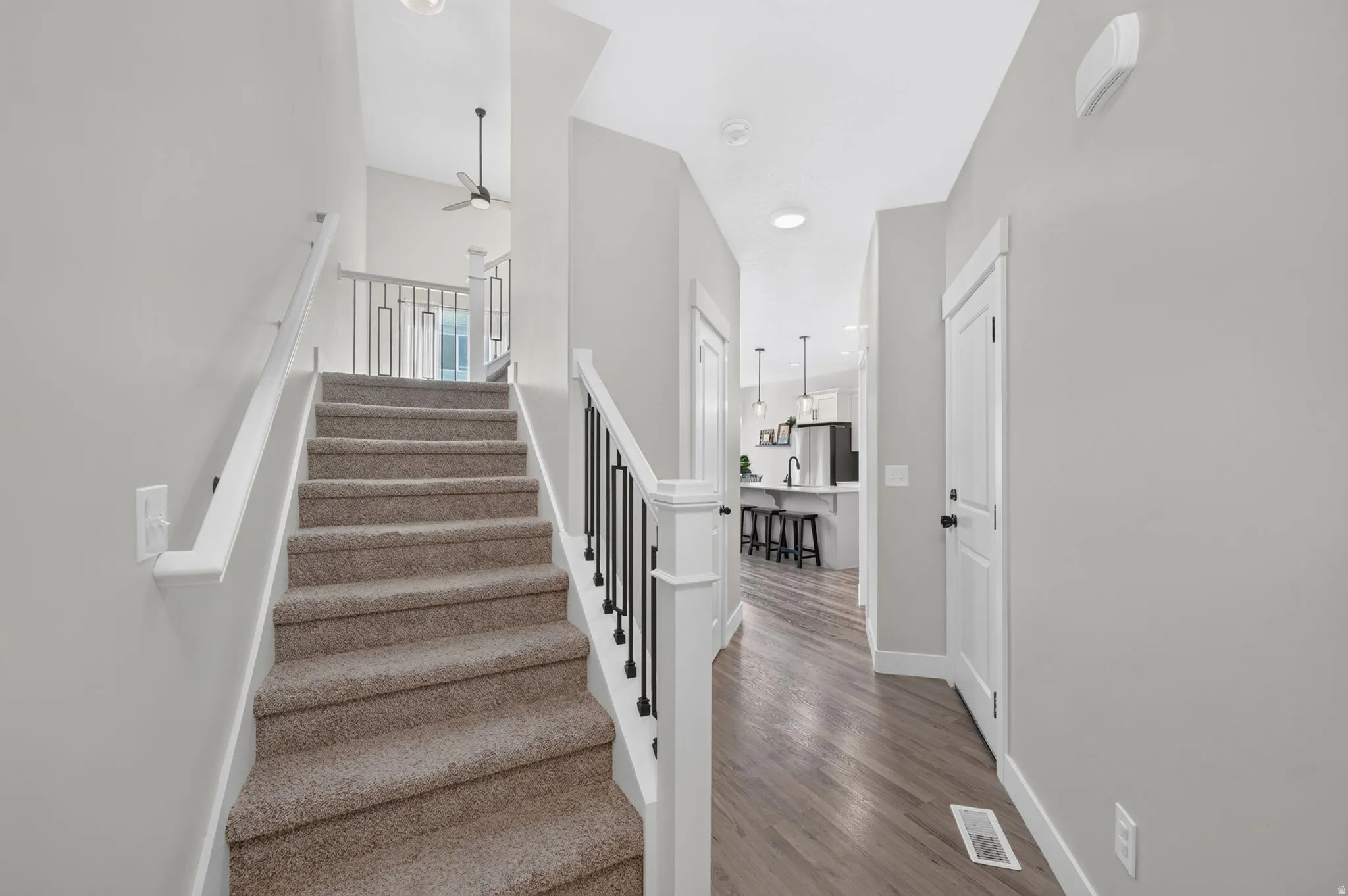 Carpeted staircase with white and black metal railings, leading to an upper level with an overhead ceiling fan