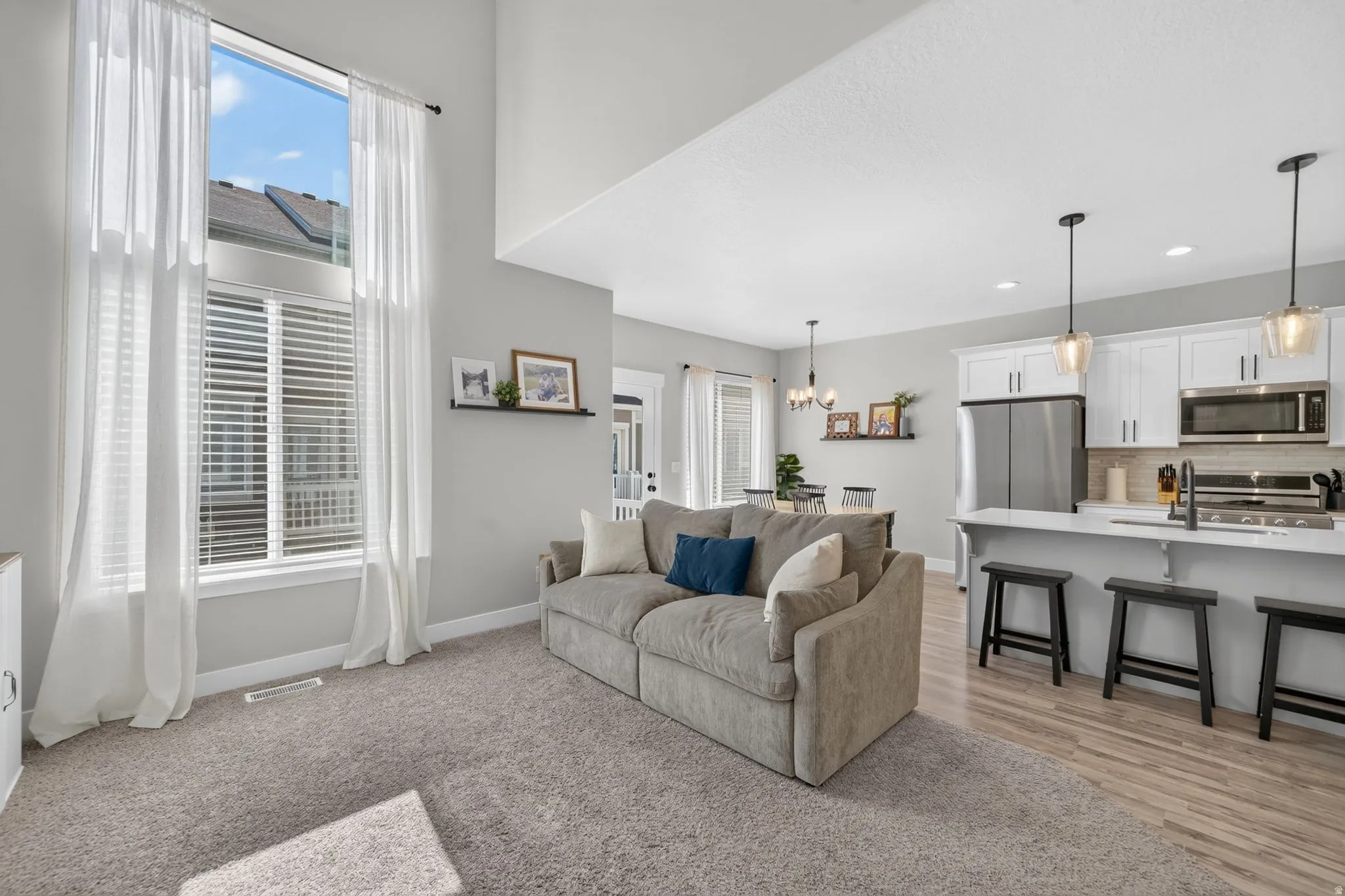 Two-story windows, vaulted ceiling, wood-finish flooring, white cabinetry, and stainless steel appliances