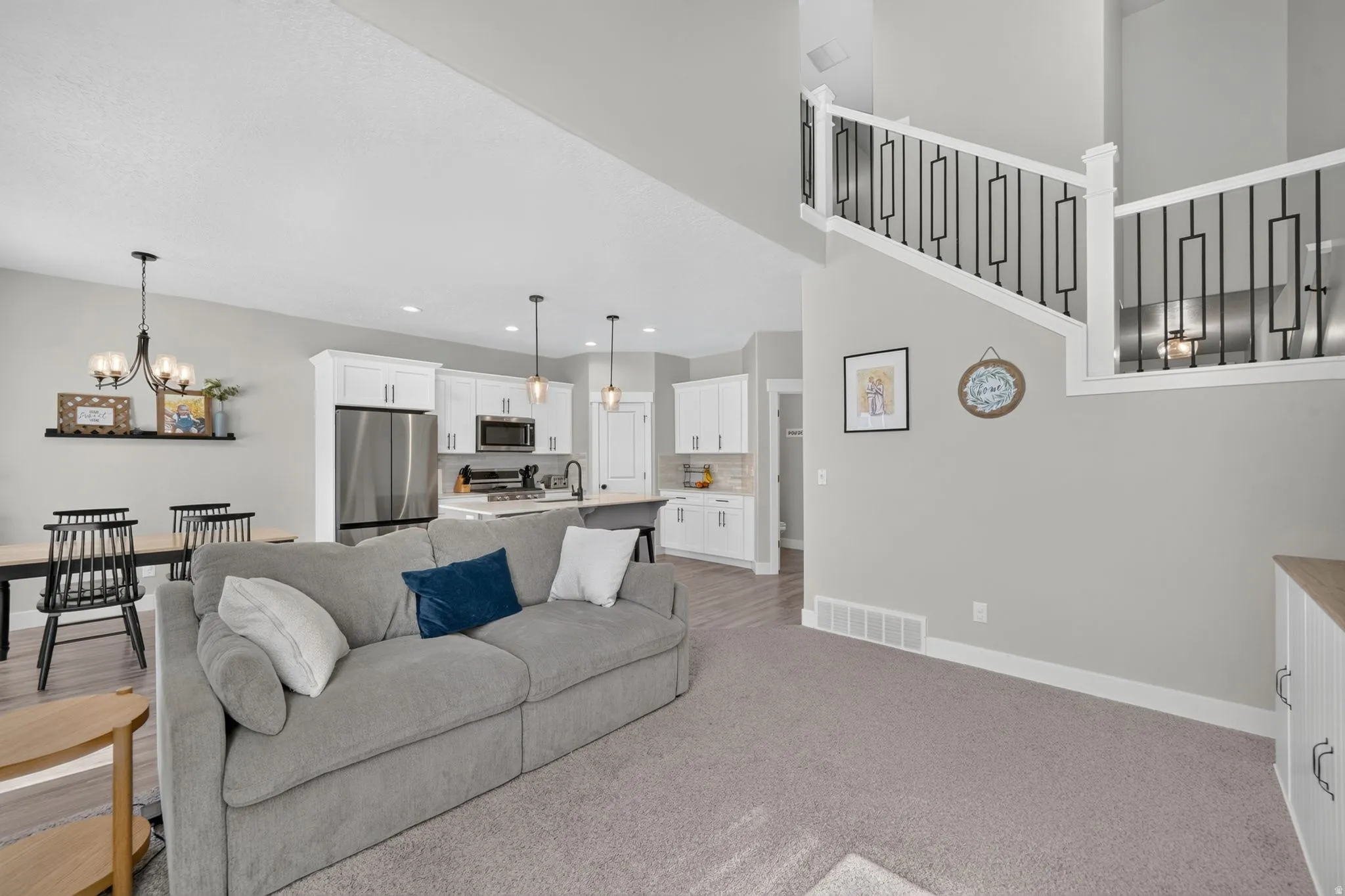 Open-concept living area featuring a kitchen with stainless steel appliances and white cabinetry, dining space with chandelier, and staircase with decorative black metal spindles