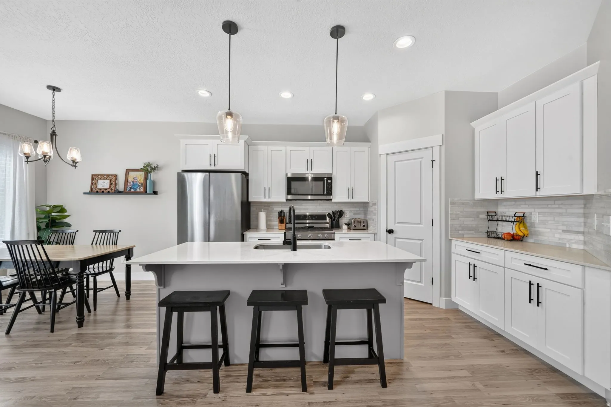 Kitchen featuring white cabinetry, light-toned countertops, stainless steel appliances, and a central island with pendant lighting