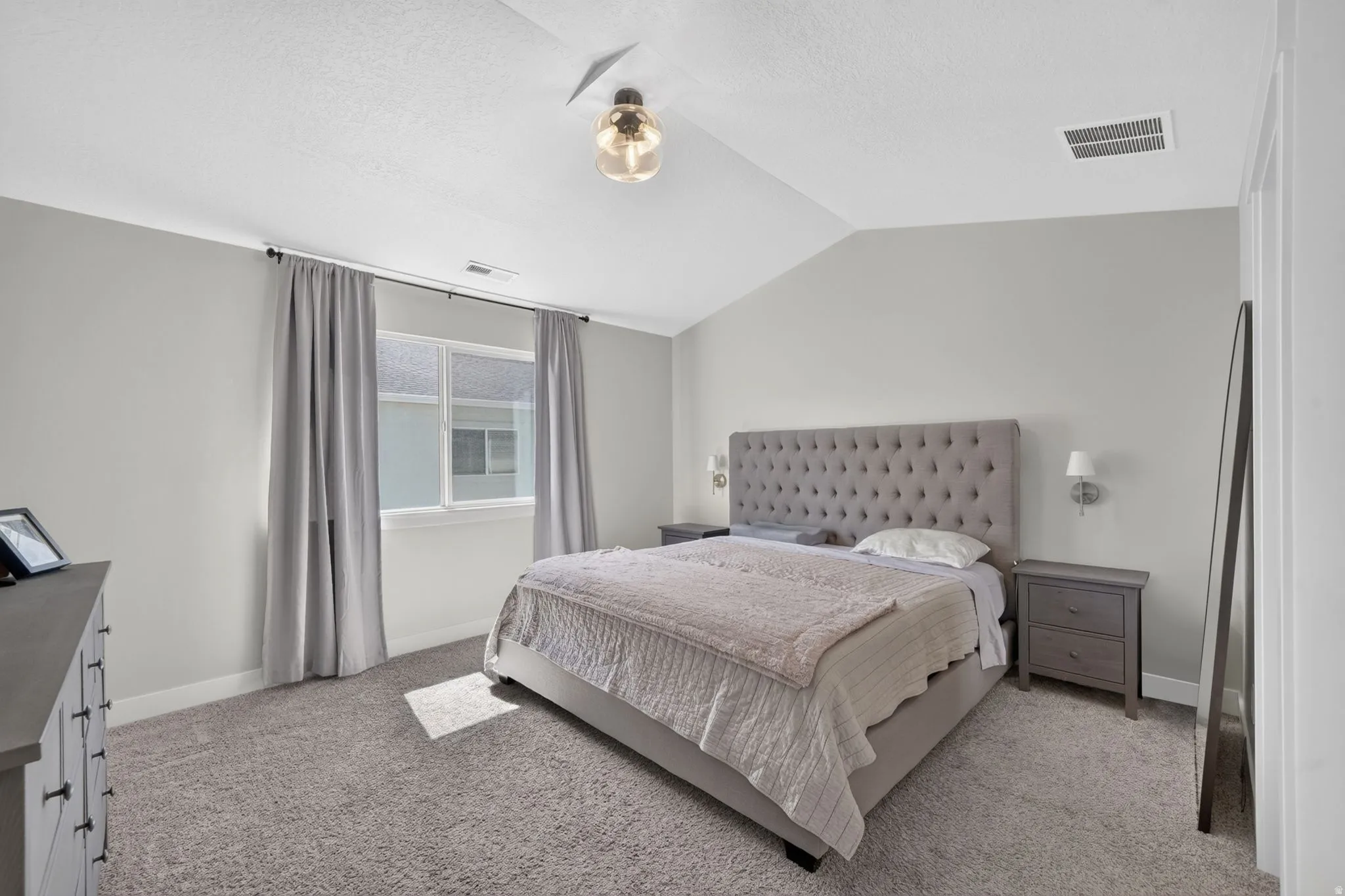 Vaulted ceiling with modern light fixture, wall-mounted sconces, and neutral wall paint