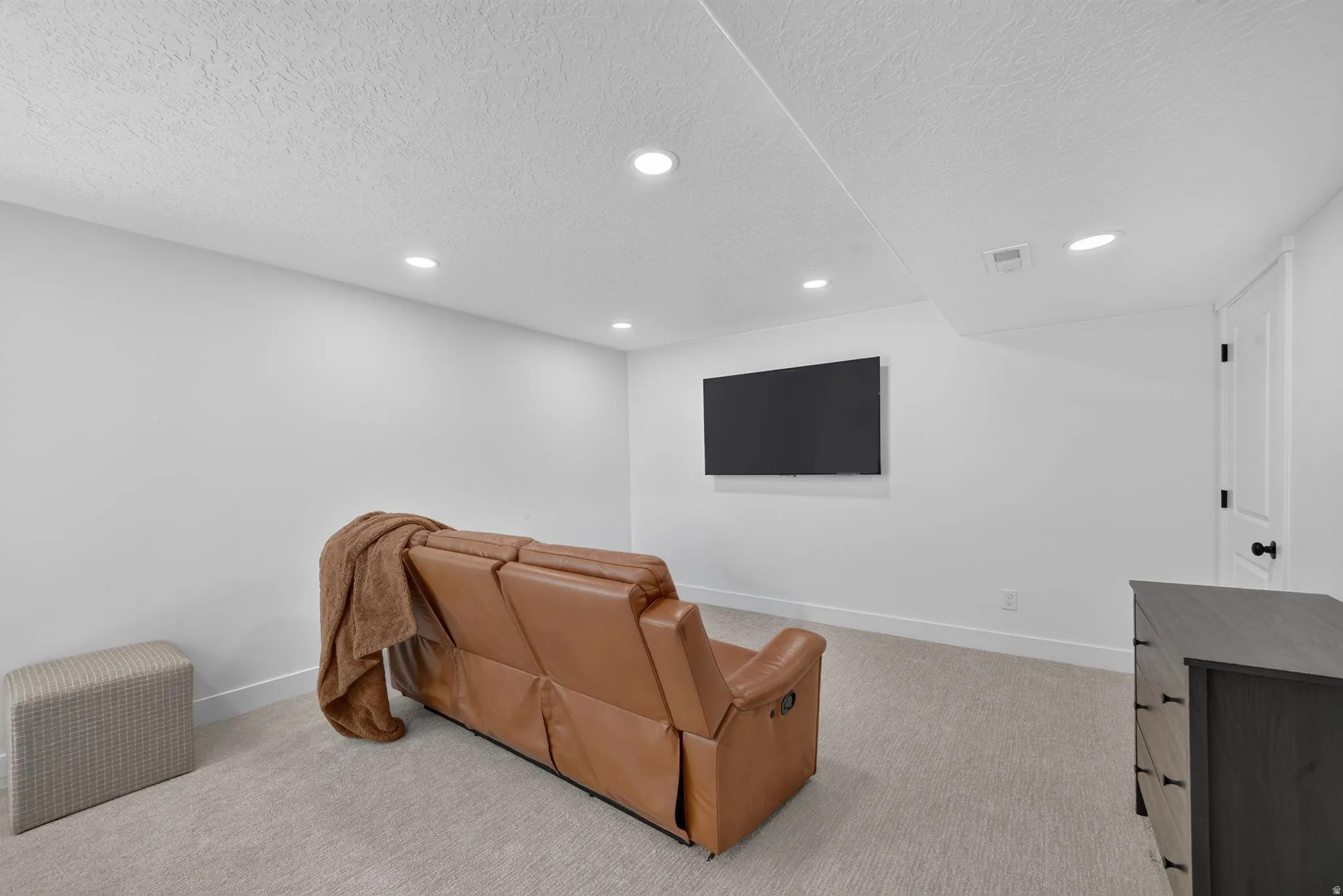 Recessed lighting illuminates this bright room featuring light-toned carpeting and white walls