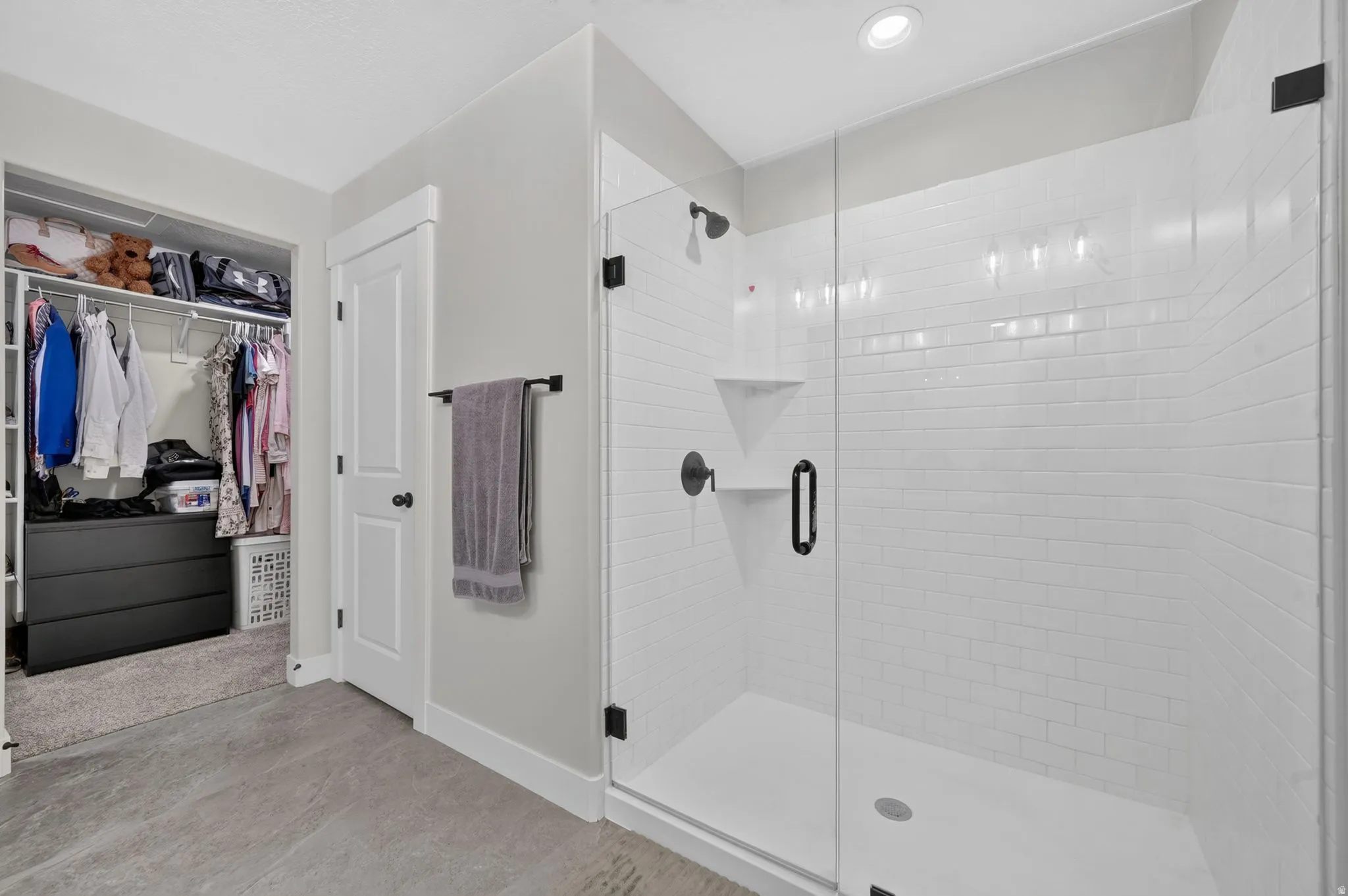 Glass-enclosed shower with white subway tile, matte black fixtures, and built-in shelving