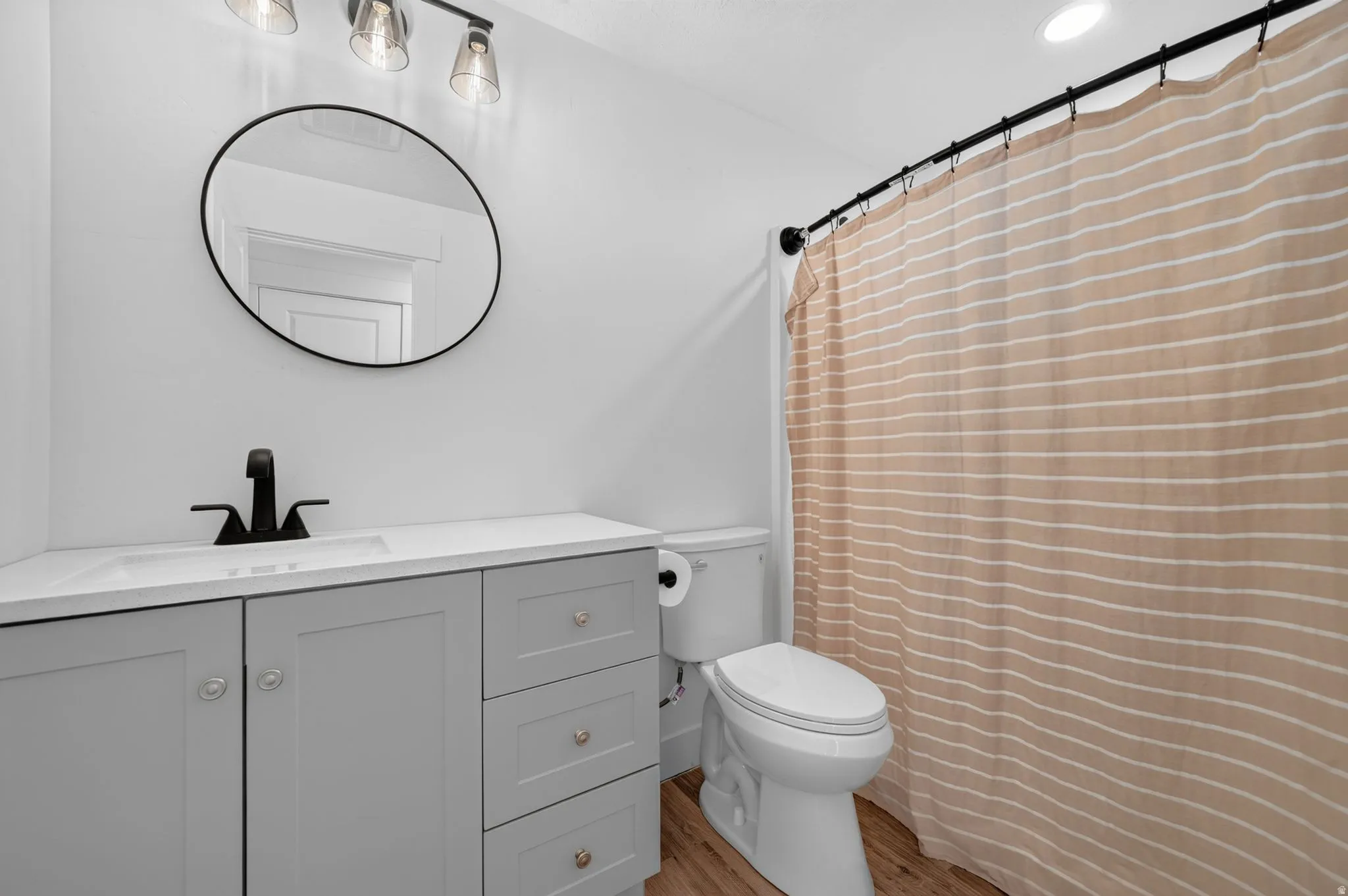 Light gray vanity with an integrated sink, matte black faucet, wood-finish flooring, and recessed ceiling lighting