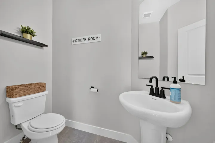 Pedestal sink with a matte black faucet, wall-mounted mirror, and tile flooring