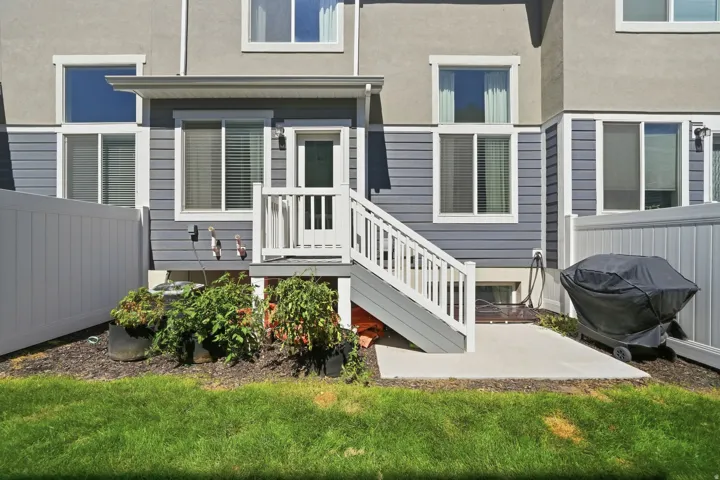 Exterior featuring gray siding and light stucco, an upper-level patio door, and white railing steps to a ground-level concrete patio