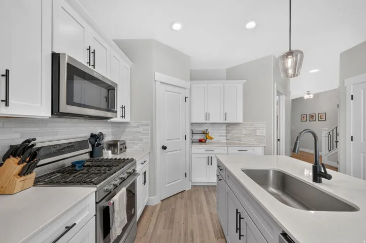 Stainless steel gas range with microwave, white shaker cabinetry, light-toned wood-finish flooring, island with undermount sink, and recessed lighting