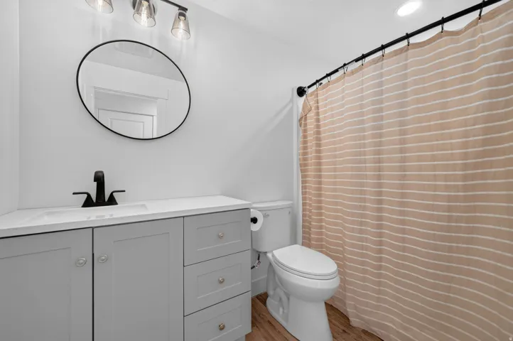 Light gray vanity with an integrated sink, matte black faucet, wood-finish flooring, and recessed ceiling lighting
