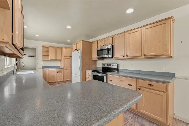 Kitchen featuring light wood cabinetry, gray countertops, stainless steel appliances, and recessed lighting