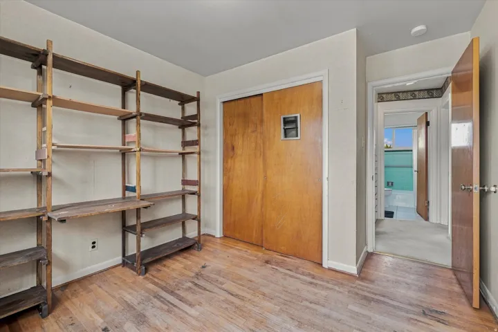 Wood-finish flooring with a built-in shelving system, sliding closet doors, and a paneled interior door