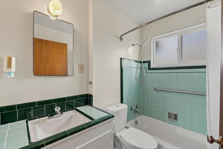 Bathroom featuring a built-in tub with shower, tiled walls, a single-pane window, and a vanity with an integrated sink