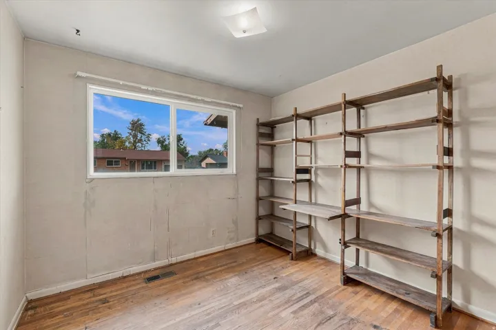 Wood-finish flooring, built-in shelving, natural light from a double window, and a ceiling-mounted light fixture