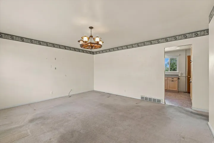 Spacious interior room with light-colored carpeting, decorative wallpaper border, and a wagon wheel-style ceiling fixture