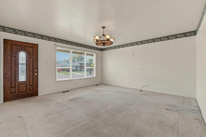 Wood-panel entry door with decorative glass inserts, large picture window with blinds, and a wagon wheel chandelier